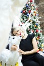 Beautiful blonde in a black dress hugs the figure of a deer near the Christmas tree Royalty Free Stock Photo