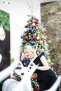 Beautiful blonde in a black dress hugs the figure of a deer near the Christmas tree Royalty Free Stock Photo