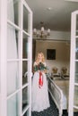 Beautiful blonde bride with bouquet of red roses standing near the window Royalty Free Stock Photo