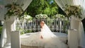 Bride in flimsy dress sitting in rotunda decorated with flowers and curtains