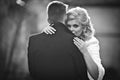 Beautiful blonde bride hugging handsome groom in black coat in t Royalty Free Stock Photo