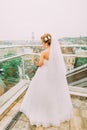 Beautiful blonde bride in white wedding dress looking down at the balcony of luxury hotel room Royalty Free Stock Photo