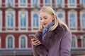 Beautiful blonde in a brown coat with fur receives SMS on a cell phone on the street. large portrait