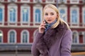 Beautiful blonde in a brown coat with fur talking on a cell phone in the street. large portrait