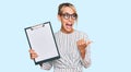 Beautiful blonde business woman holding clipboard with blank space pointing thumb up to the side smiling happy with open mouth Royalty Free Stock Photo