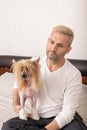 Beautiful blonde caucasian man in a white shirt is holding his lovely Chinese crested dog. Family pet, indoor activity, lifestyle