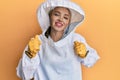 Beautiful blonde caucasian woman wearing protective beekeeper uniform excited for success with arms raised and eyes closed