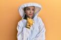Beautiful blonde caucasian woman wearing protective beekeeper uniform with hand on chin thinking about question, pensive