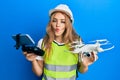 Beautiful blonde caucasian woman wearing safety hard using drone making fish face with mouth and squinting eyes, crazy and comical