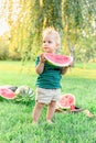 Beautiful blonde child boy eating big slice of ripe red watermelon on watermelon field at harwest. Happy childhood in summer time