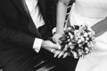 Beautiful blonde couple is sitting on wooden bench in old city. Groom in dark blue suit and bride in lace satin wedding dress are