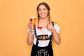 Beautiful blonde german woman with blue eyes wearing octoberfest dress drinking glass of beer happy with big smile doing ok sign, Royalty Free Stock Photo