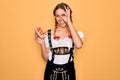 Beautiful blonde german woman with blue eyes wearing oktoberfest dress eating hot dog with happy face smiling doing ok sign with Royalty Free Stock Photo