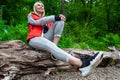 Beautiful blonde girl in a autumn jacket with a red backpack sits on a fallen tree in a forest or park in nature, walking and Royalty Free Stock Photo