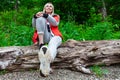 Beautiful blonde girl in a autumn jacket with a red backpack sits on a fallen tree in a forest or park in nature, walking and Royalty Free Stock Photo