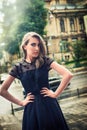 Beautiful blonde girl with big blue eyes and black dress, looking fashion with hands on the waist, in the city Royalty Free Stock Photo