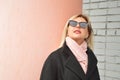 A beautiful blonde girl in a black coat, pink scarf and sunglasses looks into the distance Royalty Free Stock Photo