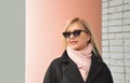 Urban portrait of a modern Caucasian blonde girl in a black coat, pink scarf and sunglasses Royalty Free Stock Photo