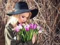 Beautiful blonde girl in a black hat is enjoying tulips bouquet Royalty Free Stock Photo