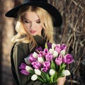 Beautiful blonde girl in a black hat is enjoying tulips bouquet Royalty Free Stock Photo