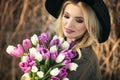 Beautiful blonde girl in a black hat is enjoying tulips bouquet Royalty Free Stock Photo