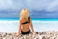 Beautiful blonde girl in a black swimwear sits on an empty Caribbean beach Royalty Free Stock Photo