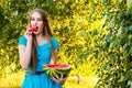 Beautiful blonde girl in blue dress eating a watermelon outdoors Royalty Free Stock Photo