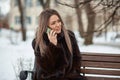 beautiful blonde girl Caucasian appearance in a fur coat sitting in a Park on a bench in the winter and talking on the Royalty Free Stock Photo