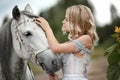 Beautiful blonde girl in dress strokes a gray horse on nature in Royalty Free Stock Photo