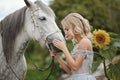 Beautiful blonde girl in dress strokes a gray horse on nature in Royalty Free Stock Photo