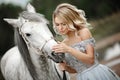 Beautiful blonde girl in dress strokes a gray horse on nature in Royalty Free Stock Photo