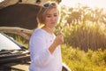 Beautiful blonde girl is engaged in repairing a car on a country road and holds a wrench and spark plugs in the rays Royalty Free Stock Photo