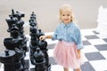 A beautiful blonde girl of five is standing next to a large chess set in the Park Royalty Free Stock Photo