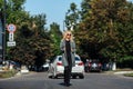 Beautiful blonde girl in a gray coat is walking on the roadway on the background of cars