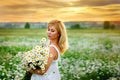 Beautiful blonde girl laughing in a field of daisies at sunset with a bouquet of camomiles Royalty Free Stock Photo