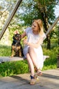 A beautiful blonde girl in a light dress with her cute dog is sitting on a park bench. Vertical view Royalty Free Stock Photo