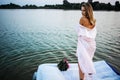 A beautiful blonde girl in a pink bathrobe stands near lake at sunset. Fairy story. Royalty Free Stock Photo