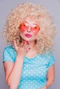 Beautiful blonde girl in retro style with a voluminous curly hairstyle, in a blue polka-dot blouse and pink glasses on a gray Royalty Free Stock Photo