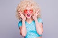 Beautiful blonde girl in retro style with voluminous curly hairstyle in a blue polka-dot blouse and pink glasses on a gray Royalty Free Stock Photo