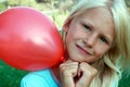 Beautiful blonde girl siting on the grass and holding a red ball