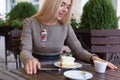 Beautiful blonde girl sitting at cafe with Cup of coffee and cake works and draws sketches in a notebook Royalty Free Stock Photo