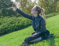 Beautiful blonde girl sitting on a green lawn and makes selfie Royalty Free Stock Photo