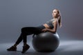 Beautiful blonde girl in sports clothes sitting on fitness ball on dark background Royalty Free Stock Photo