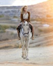 Beautiful blonde girl riding white horse in the mountain desert of Cappadocia in the rays of sunset Royalty Free Stock Photo