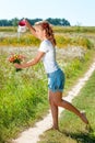 Beautiful blonde girl walking barefoot on summer field with a bouquet of wild flowers Royalty Free Stock Photo