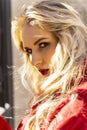 Beautiful blonde girl wearing a red coat and gloves is resting on the street in the sunlight. Close up. Trendy, commercial,