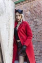 A beautiful blonde girl wearing a red coat and gloves stands at a ruined wall and brick arch near an old building. Fashionable, Royalty Free Stock Photo