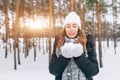 Beautiful blonde girl in white woolen hat blowing on the snow in Royalty Free Stock Photo