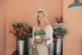 Beautiful blonde hair girl standing with confidence in front of flower in open retails flora shop. Small business owner concept