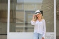 Beautiful blonde hair girl with white hat standing against wall glass as fashion pose outdoor Royalty Free Stock Photo